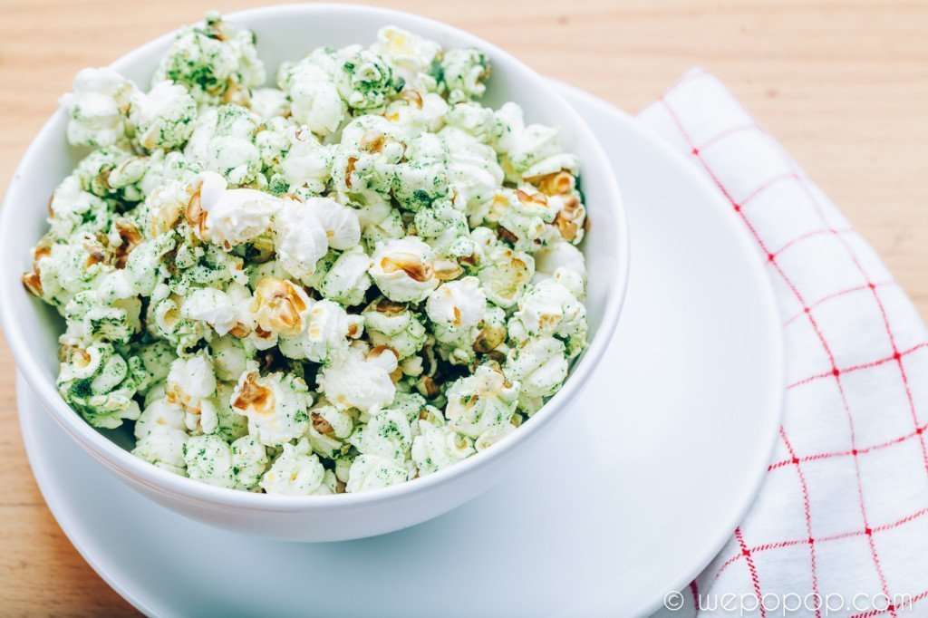 Sourcream- and onionpopcorn i en skål som står på en tallrik med en rutig handduk under