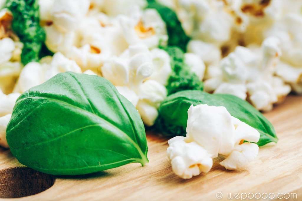 Poppade popcorn med grön pesto ovanpå och några blad färsk basilika på en skärbräda