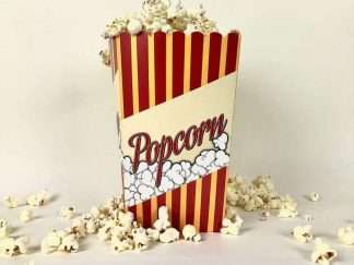 Stående popcornbägare fylld med poppade popcorn mot vit bakgrund