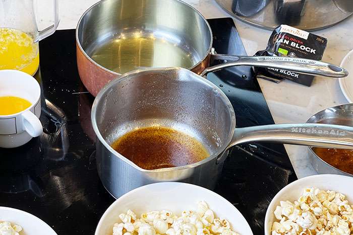 Smält veganskt smör i kastrull bredvid skålar med popcorn