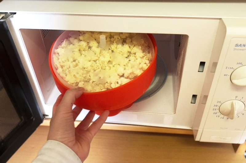 Micropopcornskål med färdiga popcorn tas ut ur mikrovågsugnen