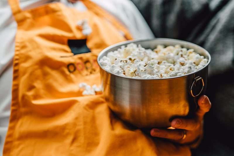 Skål med nypoppade kastrullpopcorn hålls av person i WePoPoP-förkläde